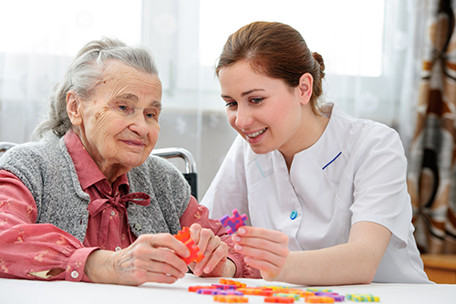 Young CNA helping elderly woman put a puzzle together